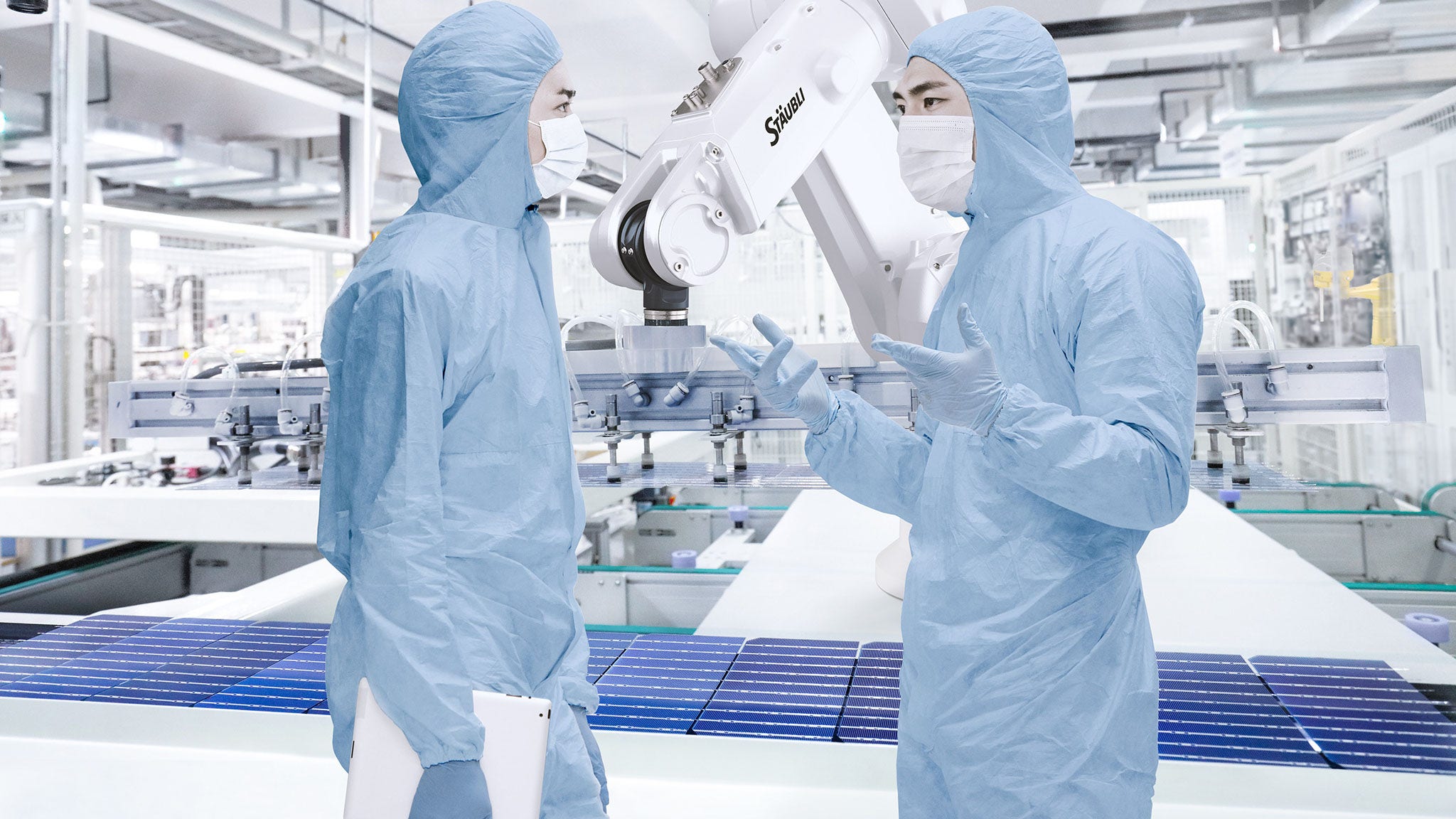 Industrial robot dedicated for solar and photovoltaic production  handles PV modules behind two operators.