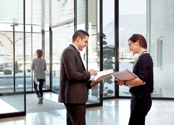 Employee of Stäubli in Faverges, France, welcomes a man in the entrance area. Picture is used on the Media-Center page of the website. It is prepared in hip (header image product page) format and edited with the brand fresh-up filter.