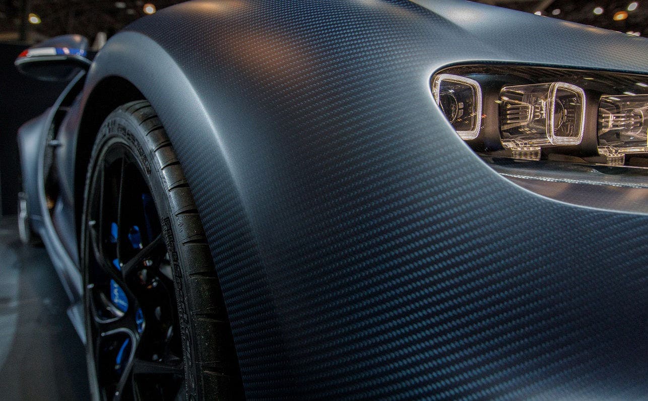 Close-up of carbon fiber body and LED headlight on front left side of luxury sports car with black alloy wheel