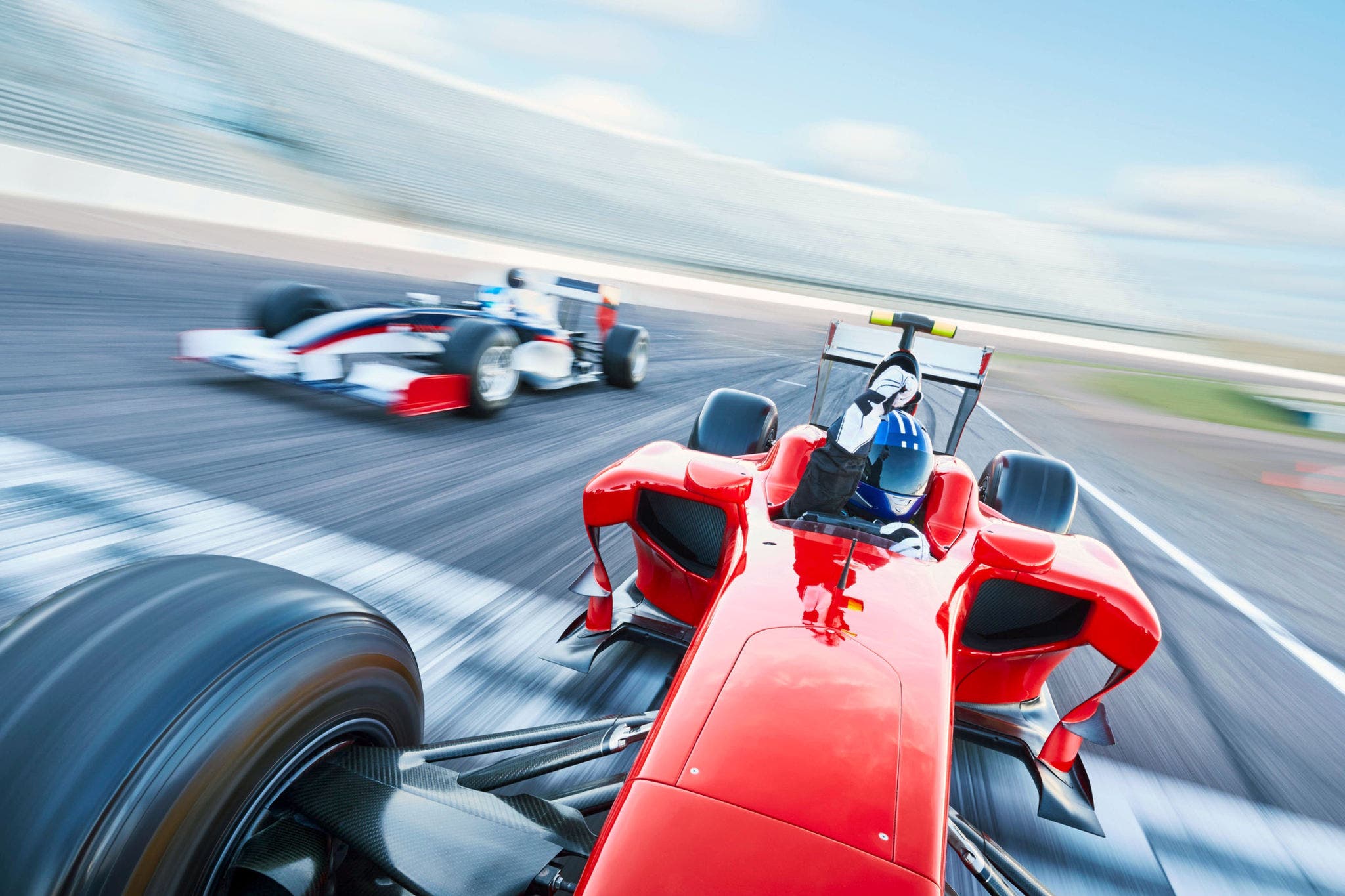 Capture the adrenaline-fueled excitement of motorsports with this vibrant image. In the foreground, powerful race cars, sleek and aerodynamic, hurtle around a sharp curve on a sun-drenched race track.; Shutterstock ID 2490660685; purchase_order: Jasmin Zehnder