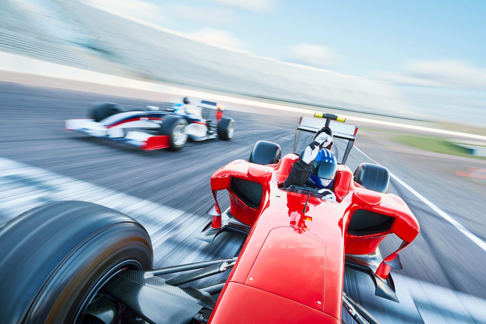 Capture the adrenaline-fueled excitement of motorsports with this vibrant image. In the foreground, powerful race cars, sleek and aerodynamic, hurtle around a sharp curve on a sun-drenched race track.; Shutterstock ID 2490660685; purchase_order: Jasmin Zehnder
