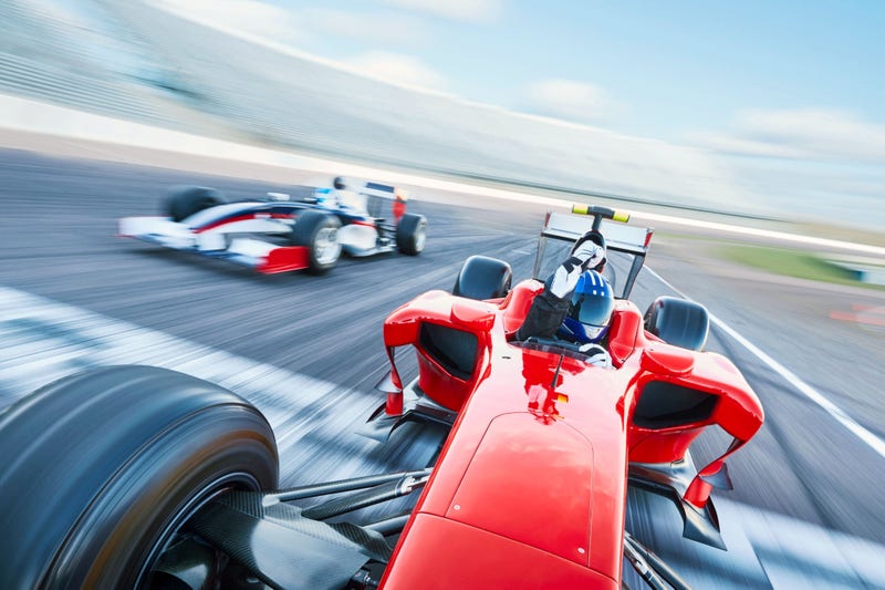 Capture the adrenaline-fueled excitement of motorsports with this vibrant image. In the foreground, powerful race cars, sleek and aerodynamic, hurtle around a sharp curve on a sun-drenched race track.; Shutterstock ID 2490660685; purchase_order: Jasmin Zehnder