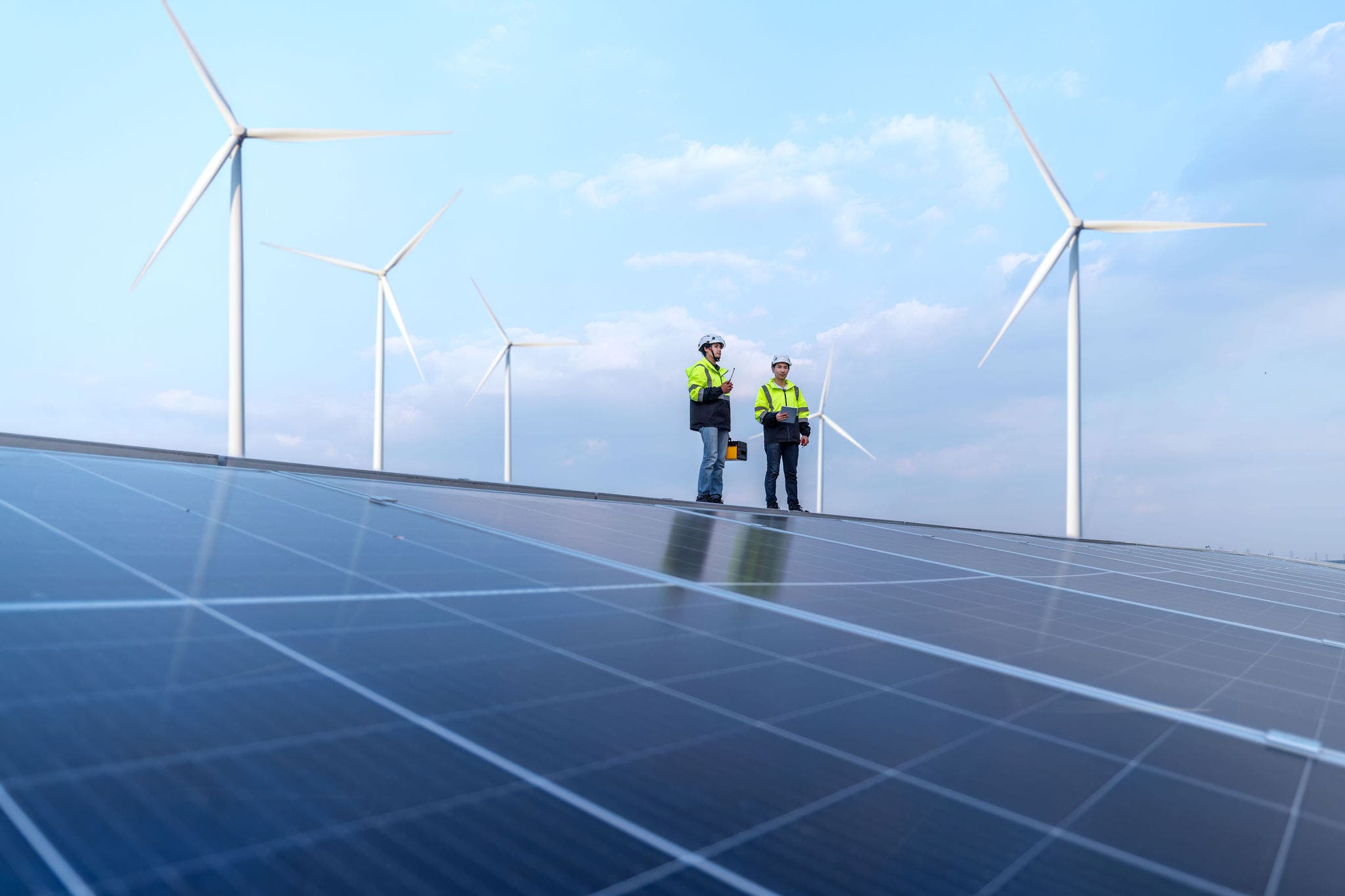 Engineers work walking on factory roof inspect survey and check solar cell panel by hold boxed with turbine wind mill field background is ecology energy alternative power factory concept.; Shutterstock ID 2455843771; purchase_order: Jasmin Zehnder