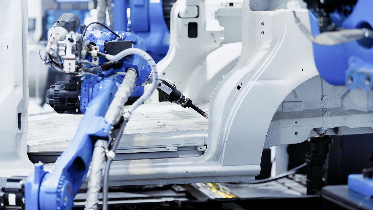 A blue robotic arm engaged in the assembly process of a white car frame in an industrial manufacturing environment.