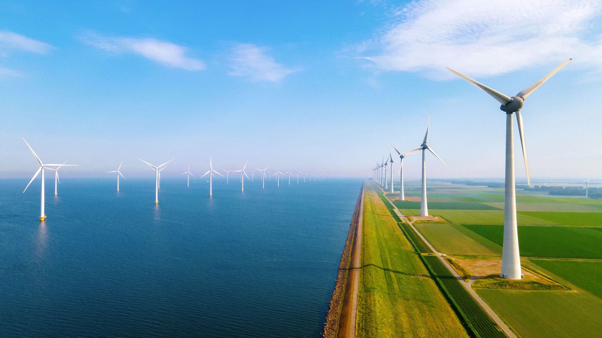 Wind turbines along coastal landscape with green fields and blue sky