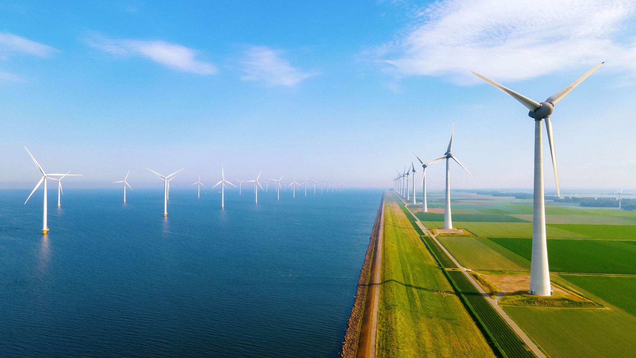 Wind turbines along coastal landscape with green fields and blue sky