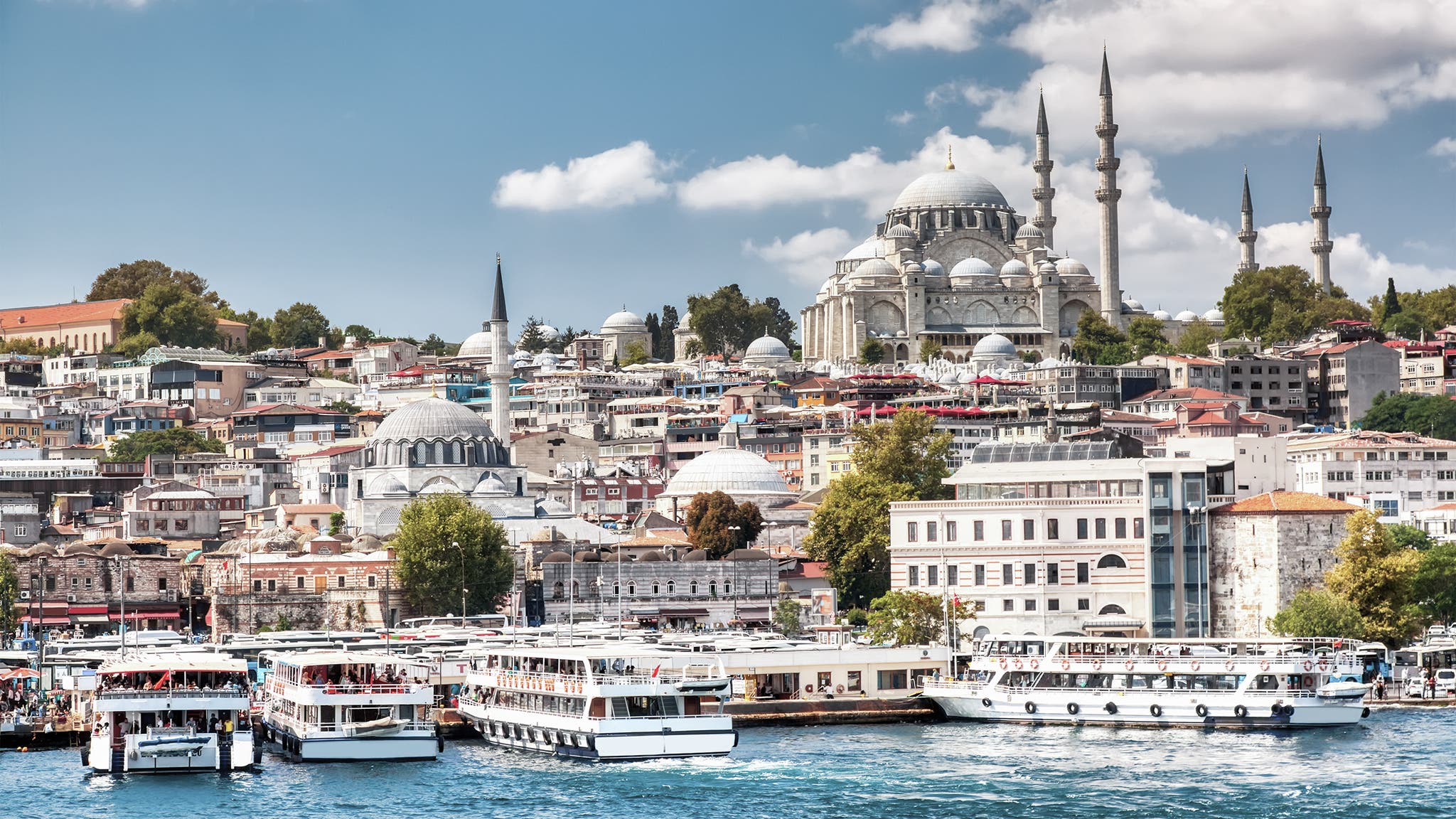 Touristic sightseeing ships in Golden Horn bay of Istanbul and view on Suleymaniye mosque with Sultanahmet district against blue sky and clouds. Istanbul, Turkey during sunny summer day.