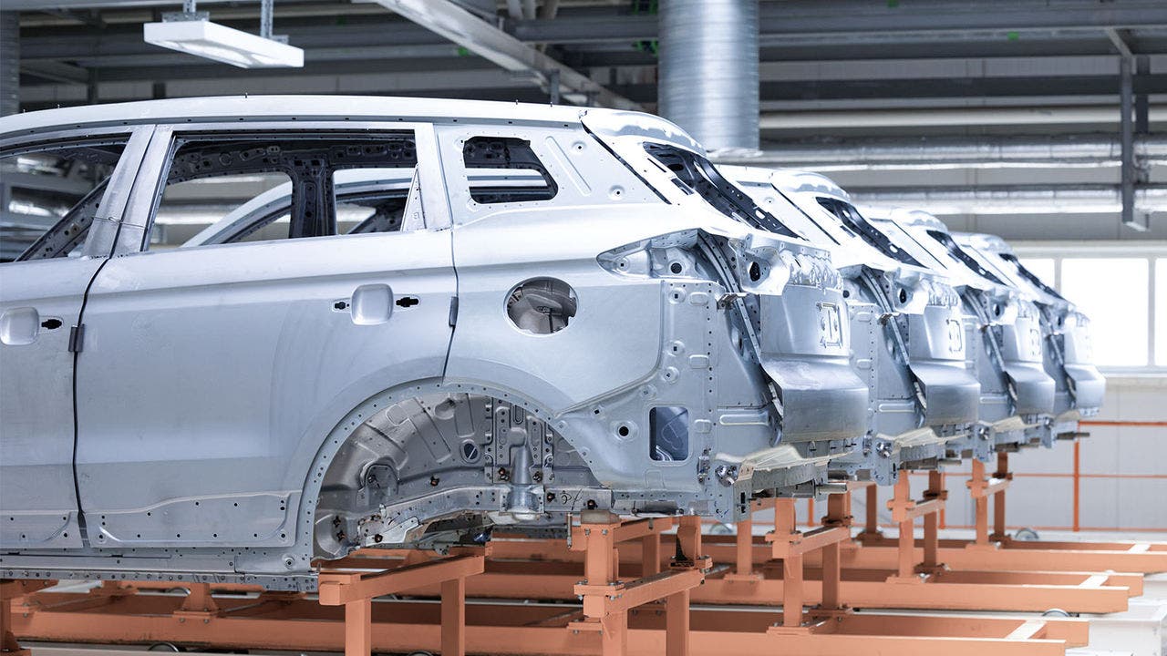 Row of unfinished car body shells aligned in a factory setting, each mounted on a platform for assembly or painting, illustrating a typical stage in automotive production.