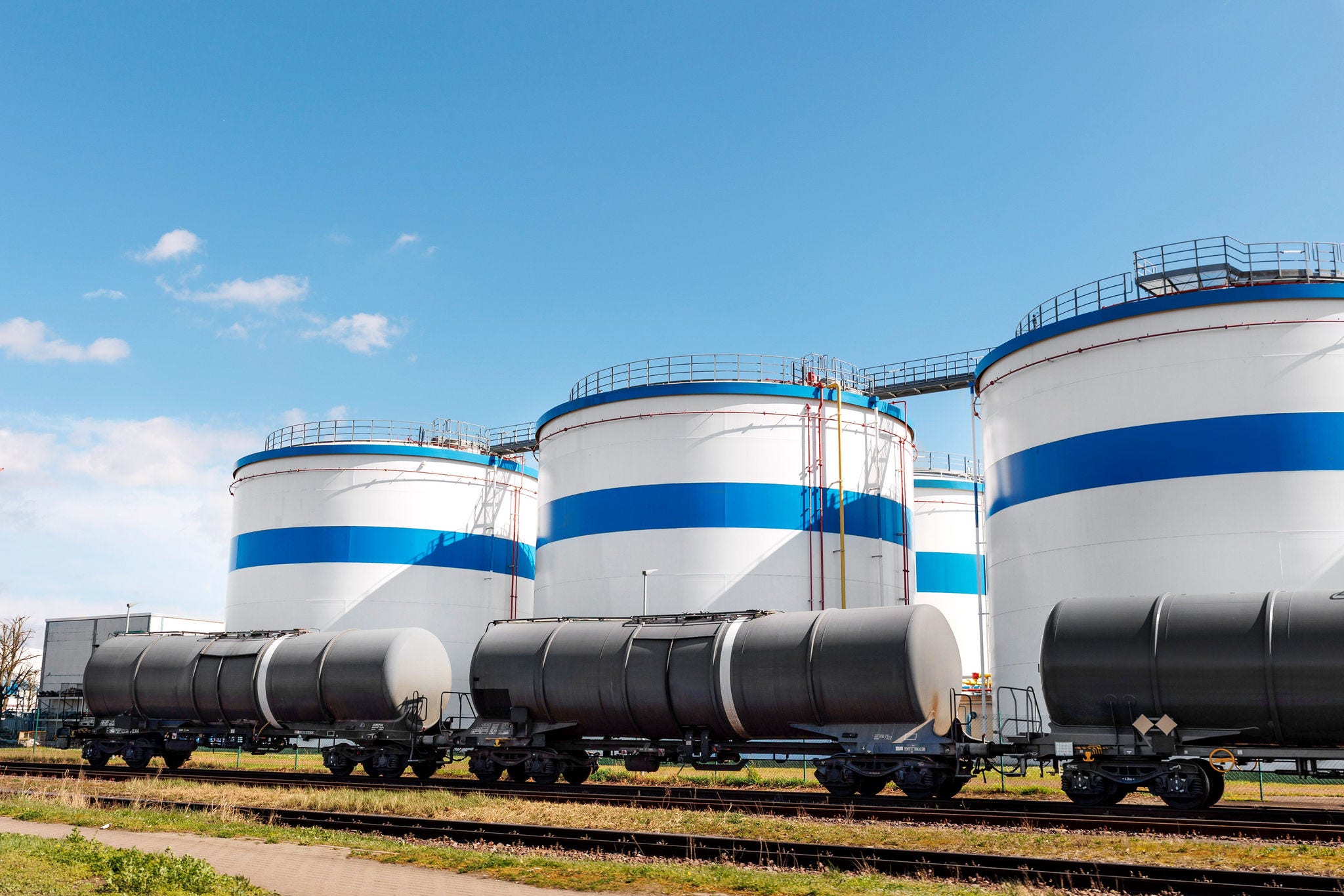 Row many large industrial fuel storage white tanks clear blue sky background on sunny day. Oil storage refinery depot liquid facilities. Energy hazmat railroad transportation storage and distribution; Shutterstock ID 2448614421; purchase_order: Patrik Gloor