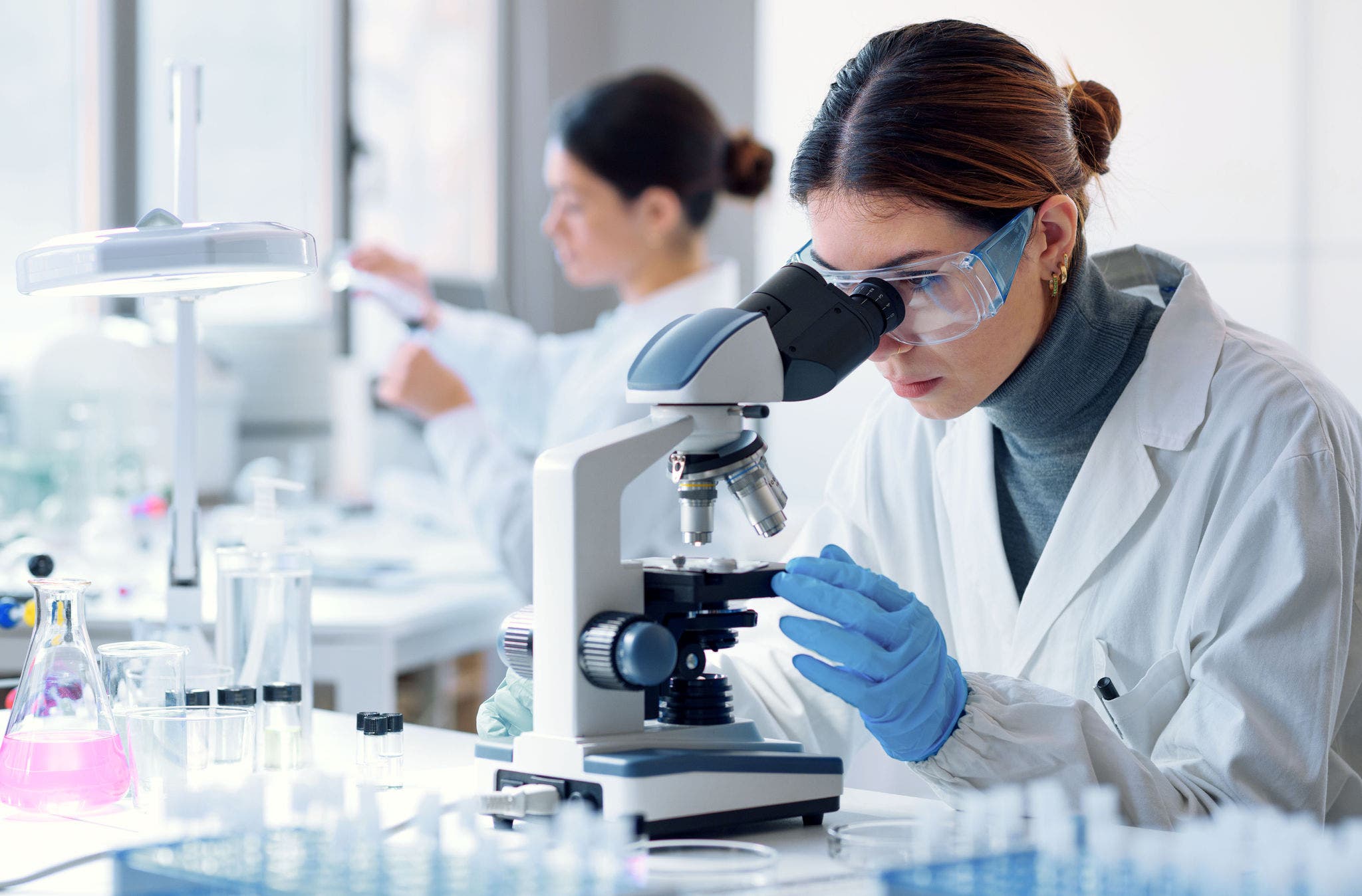 Young scientists conducting research investigations in a medical laboratory, a researcher in the foreground is using a microscope; Shutterstock ID 2149947783; purchase_order: Jasmin Zehnder
