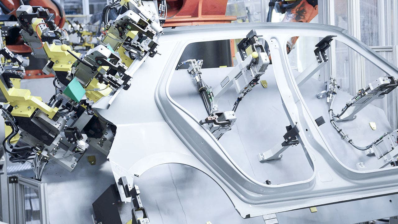 Robotic arms and machinery intricately working on a car body component in an industrial assembly line, illustrating automated precision in vehicle manufacturing technology.