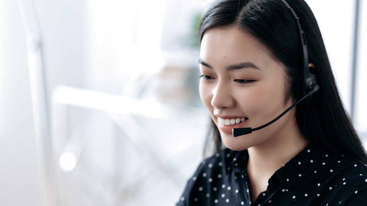 Side view of a pleasant, satisfied young asian woman with headset, freelancer, call center worker or consultant, hotline operator, smiles friendly, conducts online consultation, talks with client